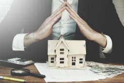 Homme joignant les mains au dessus d'une maquette de maison