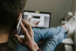 Jeune homme parlant dans un mobile devant un ordinateur