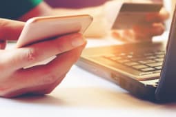 Homme tenant un smartphone et une carte bancaire devant un ordinateur