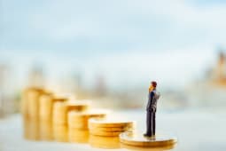 Miniature d'un homme se tenant sur une pile de pices avec la ville en arrire-plan