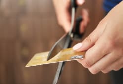 Mains coupant une carte bancaire avec une paire de ciseaux