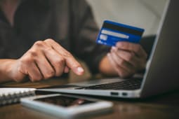 Un homme tient une carte bancaire devant un cran d'ordinateur