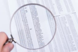 Homme utilisant une loupe pour lire une liste de chiffres