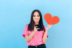 Une femme consulte un smarphone, un coeur dans la main