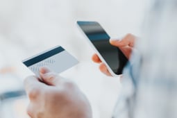 Un jeune homme consulte son mobile et tient une carte bancaire