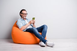 Un homme souriant consulte son smartphone assis sur un pouf