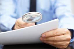 Un homme en costume lit un document avec une loupe