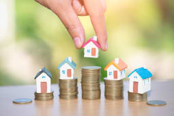 Une main dpose une maison sur une pile de pices