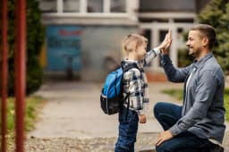 Un pre et son enfant se tapent dans la main devant l'cole