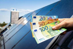 Des panneaux photovoltaques sur le toit d'une maison et une personne tenant des billets.