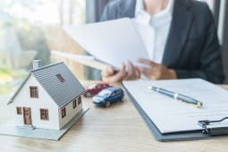 Une femme tient un contrat  ct d'une voiture et maison miniatures