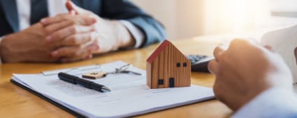 Deux personnes  un bureau autour de documents et d'une maison miniature.