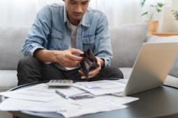 Un homme devant son ordinateur regarde son portefeuille vide.