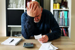 Un homme se prend la tte dans les mains en regardant un document avec une calculatrice  ct. 