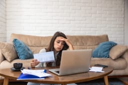 Une femme devant son ordinateur regarde des documents en soupirant. 