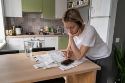 Une femme regarde des factures dans sa cuisine. 