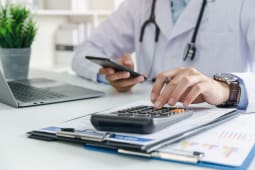 Un mdecin devant son ordinateur avec une calculatrice.