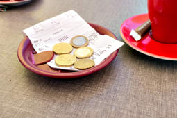 Des pices de monnaie et un billet laiss  ct d'une tasse  caf et d'un ticket de caisse.