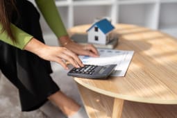 Une maison miniature  ct d'une personne utilisant une calculatrice.