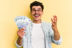 Un jeune homme tient plusieurs billets de 20 euros l'air content.
