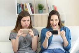 Deux femmes regardent leur tlphone, l'une joyeuse l'autre triste.