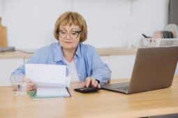 Une femme regarde son ordinateur avec une calculatrice. 