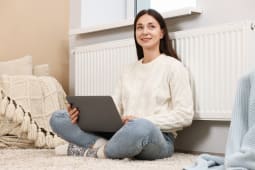 Une femme assise devant son radiateur avec un ordinateur.