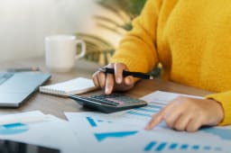 Une personne tient une calculatrice et regarde des documents.