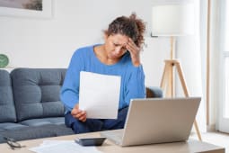 Une femme regarde son ordinateur et des documents l'air proccup.