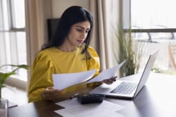 Une femme regarde son ordinateur et des documents.