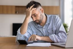 Un homme regarde une calculatrice l'air inquiet.