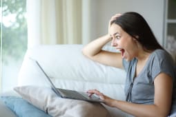 Une femme regarde son ordinateur l'air surpris