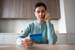 Une femme au tlphone regarde sa carte bancaire.