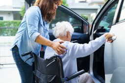 Une femme aide une personne ge  monter dans une voiture.