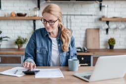 Une femme regarde son ordinateur et des documents.