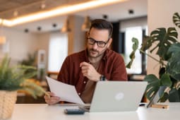 Un homme regarde son ordinateur et des documents.