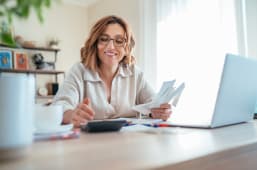 Une femme regarde des documents devant son ordinateur.