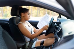 Une femme au volant d'une voiture avec des documents.