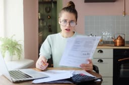 Une femme regarde son ordinateur et des documents l'air surpris.