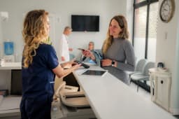Une femme enceinte effectue une transaction de paiement sans contact au comptoir d'accueil d'une clinique mdicale moderne, interagissant avec la rceptionniste pendant qu'un mdecin se promne en arrire-plan