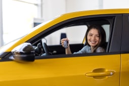 Femme souriante tenant des cls dans une voiture jaune.