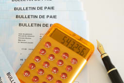 Calculatrice sur bulletins de paie avec stylo.