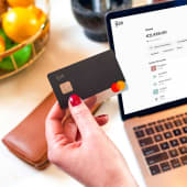 Main tenant une carte bancaire devant un ordinateur portable.