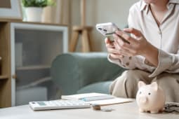 Quelqu'un tenant un tlphone portable  ct d'une calculatrice et d'une tirelire.