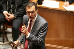 Homme en costume parlant au micro dans une salle formelle. Farandou