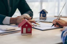 Signature de documents immobiliers avec des maisons miniatures.