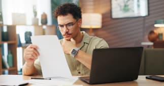 Un homme regarde un document devant son ordinateur.