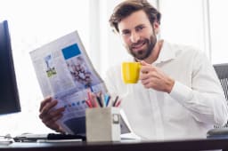 Homme souriant lisant un journal avec tasse de caf.