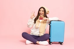 Une femme souriante  ct d'une valise avec une carte bancaire.