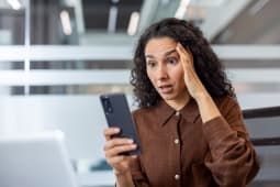 Une jeune femme dans un bureau lisant un message sur son smartphone et ragissant avec surprise.